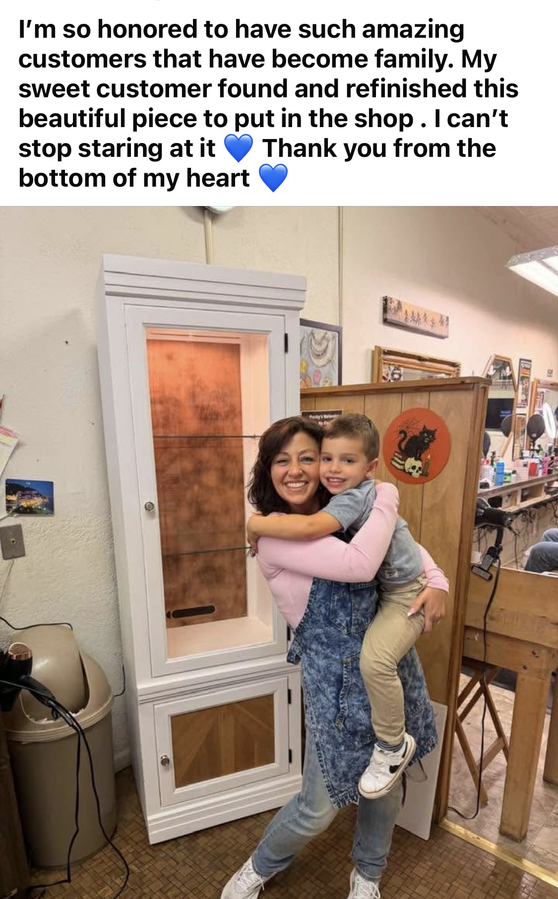 Crissy hugging a young customer beside a beautifully refinished piece gifted to Rocky's Barbershop